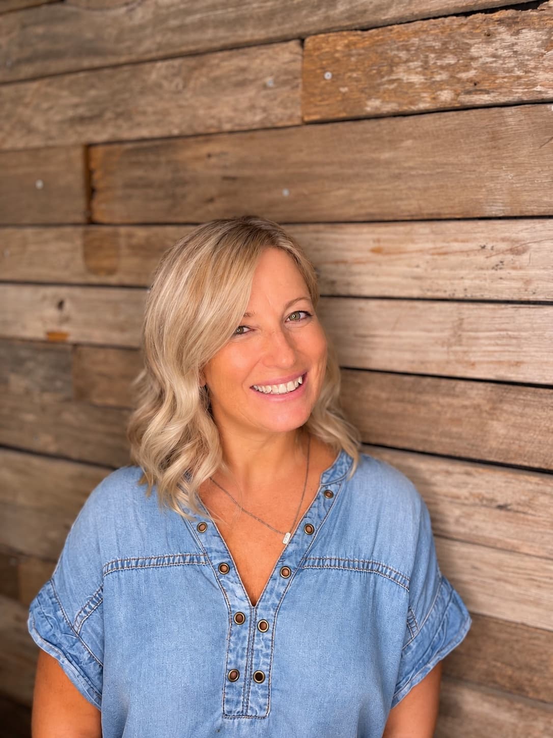 Nerilee smiling in a denim shirt against a rustic timber wall